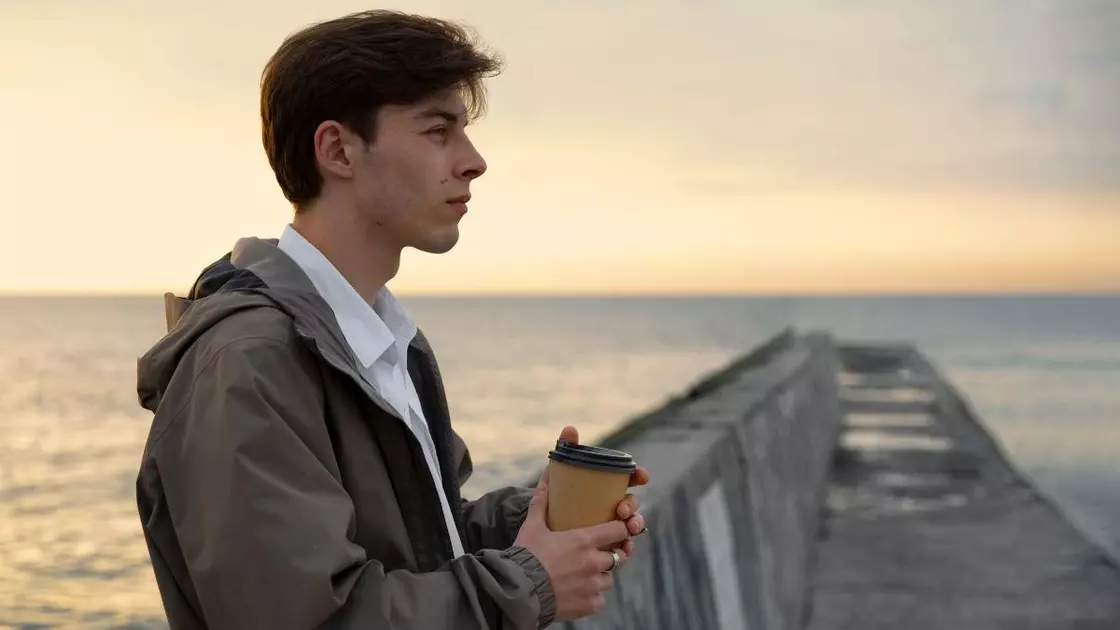 Хлопець стоїть на пірсі з кавою в руках і дивиться вдалину